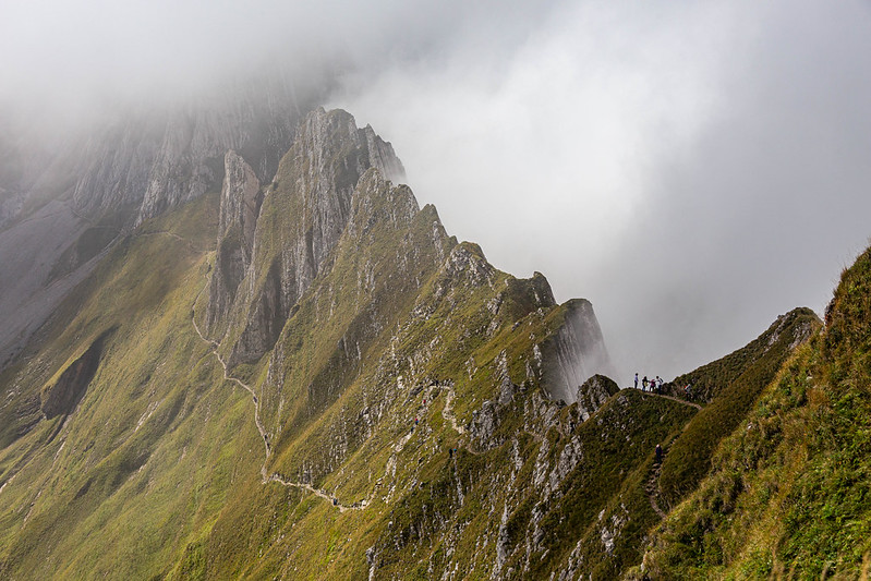 A photo of a hiking trail below a steep ridge in the clouds